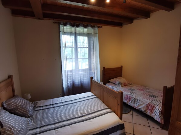 A bedroom with a large bed, a smaller bed, and a window with curtains.