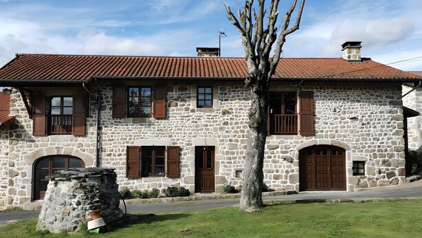 A stone building with a tiled roof, multiple windows with shutters, and a small tree in the foreground. - Gîte du Platane, Sleeps 14 (Grazac)