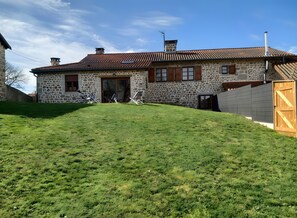 Une maison en pierre avec un toit en tuiles, une cour gazonnée et un portail en bois.