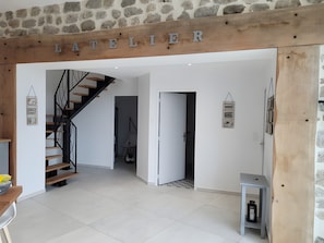 Un intérieur moderne avec un escalier, une poutre en bois portant l’inscription « L’ATELIER », et une petite table sur laquelle est posée une lanterne.
