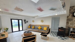 Una sala de estar moderna con un sofá, una silla de madera, una mesa redonda de centro, una chimenea y un ventanal grande.