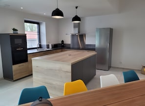 Une cuisine moderne dotée d’un îlot central, de luminaires suspendus noirs, d’un four encastré et d’un réfrigérateur.