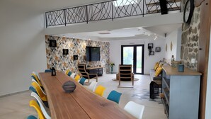 Un comedor moderno con una mesa de madera larga, sillas coloridas, una cocina con pared de piedra y un balcón con barandilla de metal.