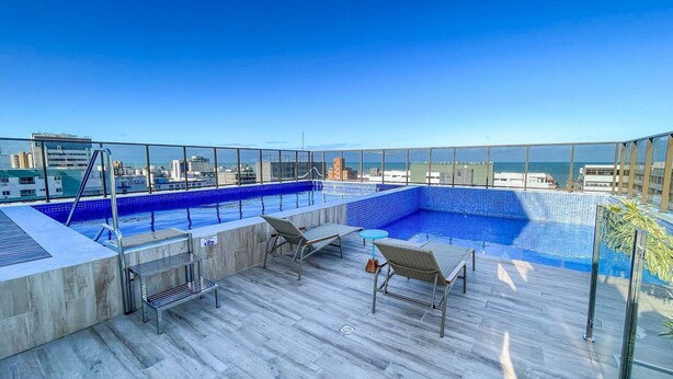 A rooftop infinity pool with a city view, lounge chairs, and a small table. - Compact Tambau #704 - Apartment By Carpediem (João Pessoa)
