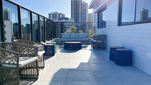 A rooftop terrace with a sofa, chairs, and round tables, offering a city view. - Compact Tambau #704 - Apartment By Carpediem (João Pessoa)