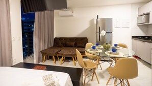 A modern hotel room with a glass dining table, a sofa, and a kitchenette. - Compact Tambau #704 - Apartment By Carpediem (João Pessoa)