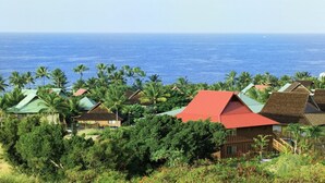 A coastal resort with multiple buildings, some with red roofs, surrounded by lush greenery and palm trees, overlooking the ocean. - Gorgeous 2 bdrm presidential unit (Kailua-Kona)