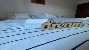Un lit bien fait, recouvert d’une couvre-lit à rayures, et sur lequel est posé un petit panneau en bois sur lequel on peut lire le mot « rêve ».