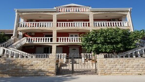 Un immeuble à plusieurs étages, doté d’une façade rouge, de balcons blancs et d’un escalier en pierre menant à l’entrée.