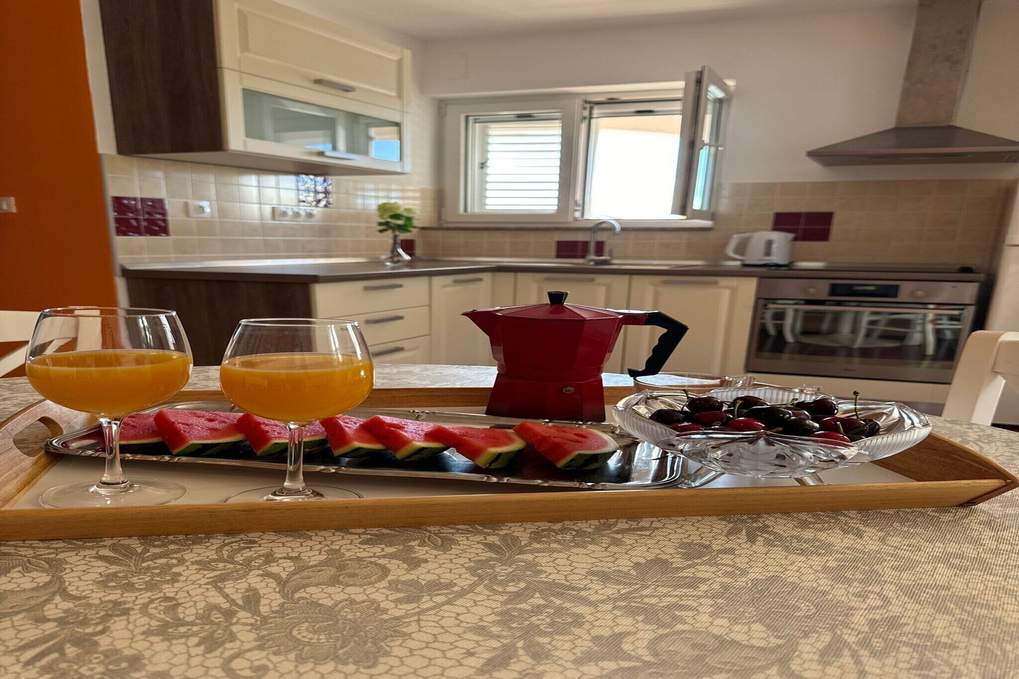 Un plateau de petit-déjeuner avec des tranches de pastèque, des cerises et des verres de jus d’orange, dans une cuisine moderne.