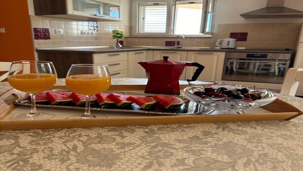 Un plateau de petit-déjeuner avec des tranches de pastèque, des cerises et des verres de jus d’orange, dans une cuisine moderne.