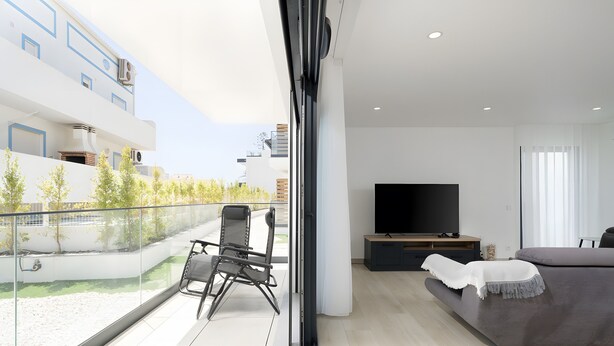 Una sala de estar moderna con un televisor grande, un sofá y un balcón con una silla.
