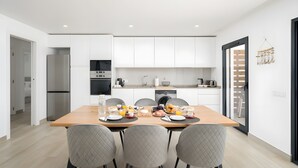 Una cocina moderna con armarios blancos, una mesa de comedor con platos, tazones y un frutero.