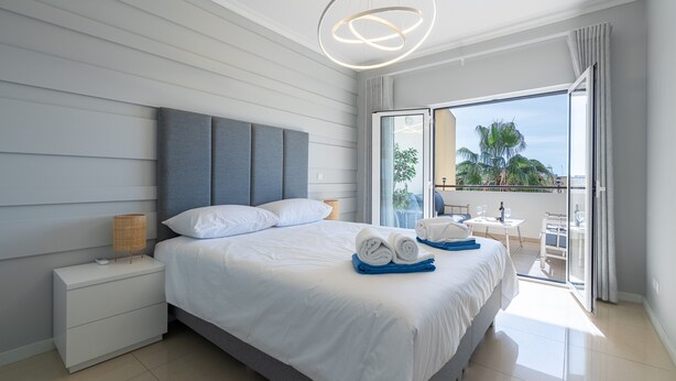 Une chambre d’hôtel moderne avec un grand lit, une table de chevet, une lampe et un balcon avec vue.