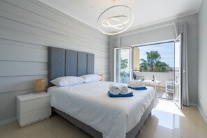 Una habitación de hotel moderna con una cama grande, una mesita de noche, una lámpara y un balcón con vistas.