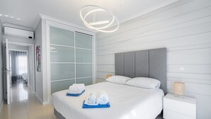 Une chambre d’hôtel moderne dotée d’un grand lit, d’un dressing, d’une table de chevet et d’un luminaire suspendu.