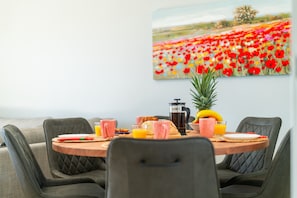A dining area with a round table, chairs, breakfast items, and a painting of a flower field on the wall. - Entire Apartment in Guia, Portugal (Guia)