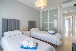 A hotel room with two beds, a large window with frosted glass, a modern light fixture, and a visible door leading to another room. - Entire Apartment in Guia, Portugal (Guia)