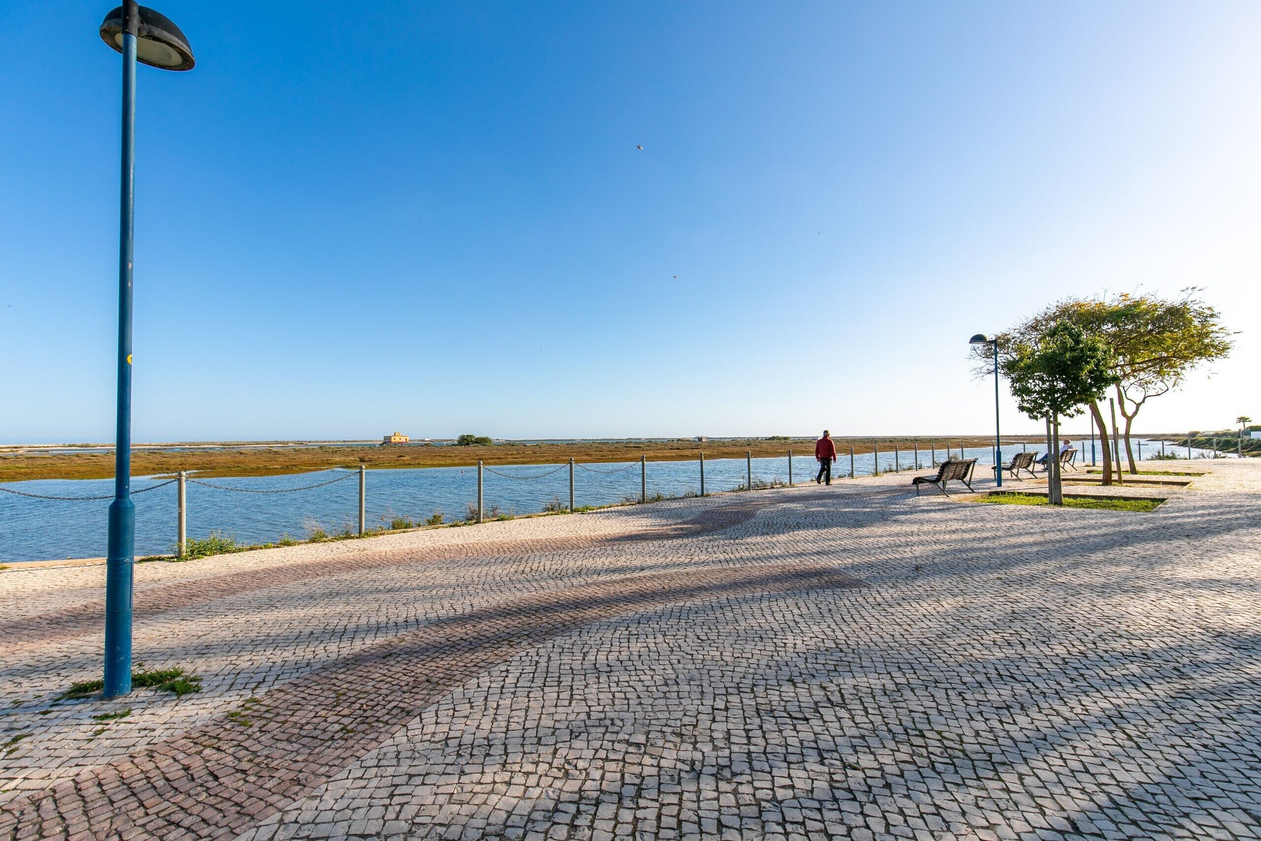 A paved walkway by a body of water with benches and a lamp post.