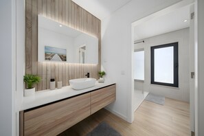 Une salle de bain moderne avec un grand miroir, un meuble-lavabo en bois et une vue sur la mer.