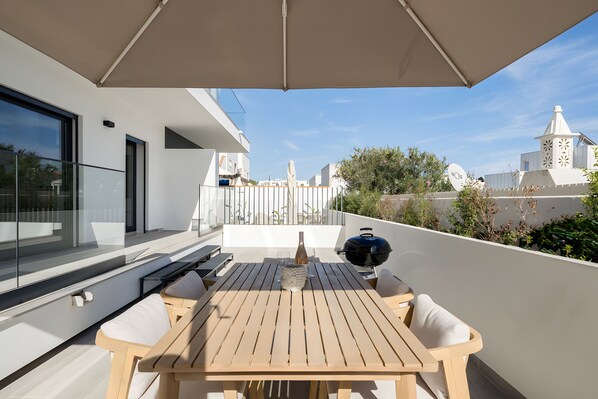 Eine Terrasse mit Tisch, Stühlen, einem Grill und einer Flasche.