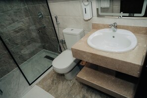 A bathroom with a glass shower enclosure, a toilet, and a sink with a mirror above it.