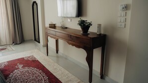 Ein Zimmer mit einem Holzkonsolentisch, einem Flachbildfernseher, einer Topfpflanze, einem rot-weißen Teppich mit Muster und einer großen Stehlampe.