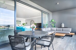 A modern living room with a round table, wicker chairs, a grey sofa, and a TV. - Luxury 2-Bedroom Apartment with Sea View and Pool (Portimão)