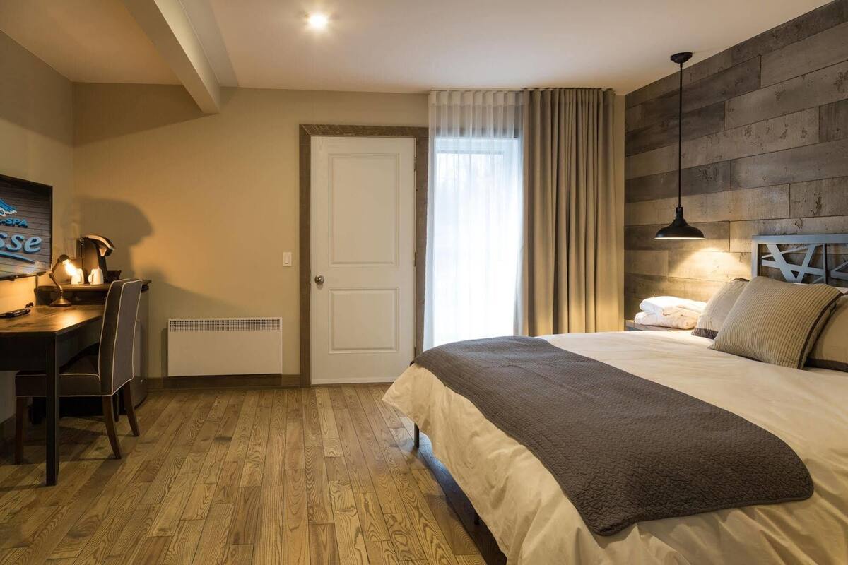 Un dormitorio con cama, escritorio con silla, ventana con cortinas y una lámpara fijada a la pared.
