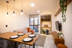 Ein modernes Wohnzimmer mit Essbereich, einer Couch, einem Fernseher und einer Pflanze.