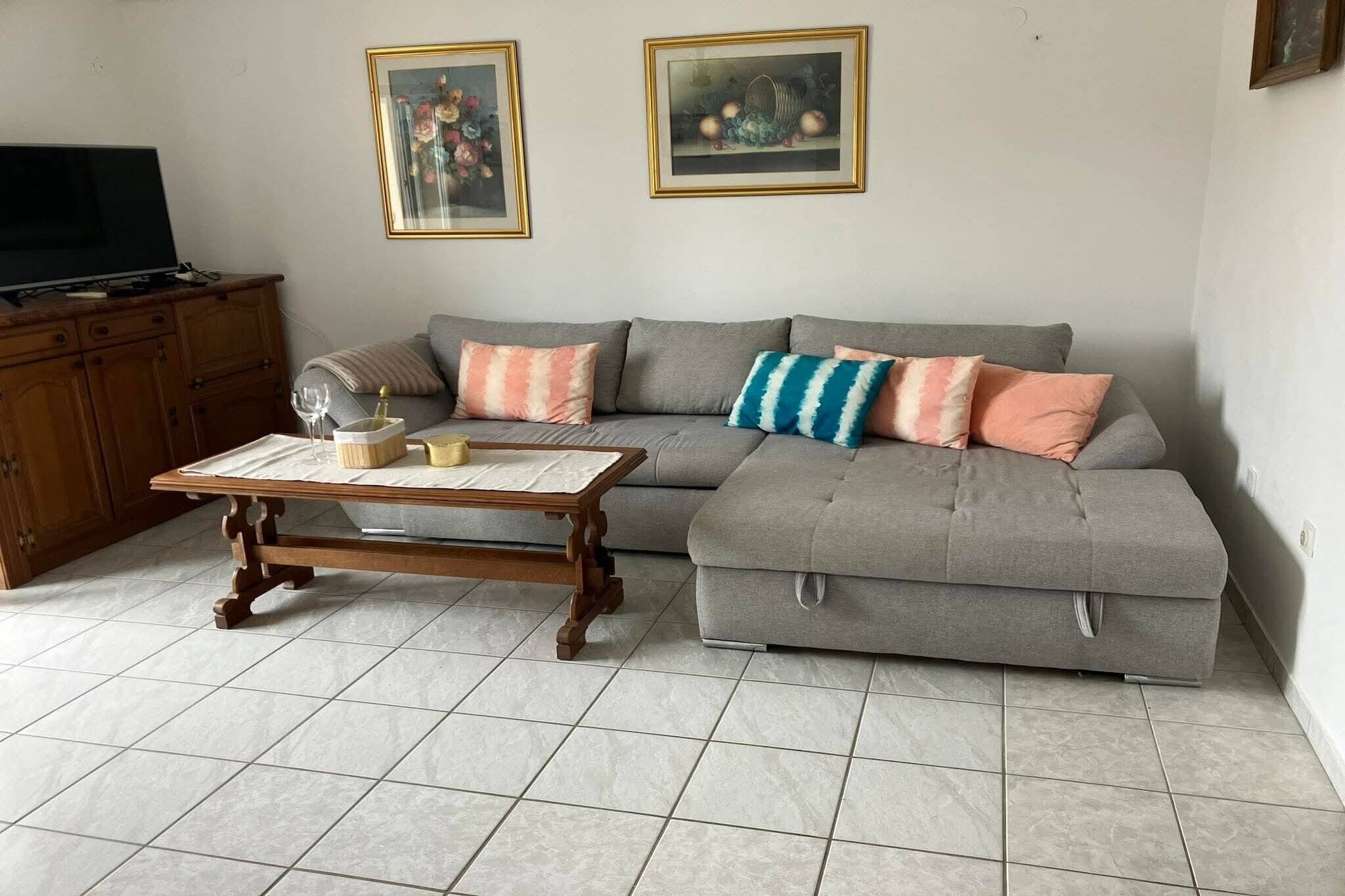 A living room with a grey sectional sofa, a wooden coffee table, a television on a wooden cabinet, and two framed pictures on the wall.