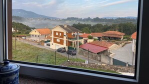 A view from a window overlooking a residential area with houses, a road, and a mountainous landscape in the distance. - Enjoy our heated swimming pool, both in summer and winter. (Ponte de Lima)