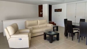 A modern living room with a beige sofa, a small coffee table, and a dining area with a black table and chairs. - Enjoy our heated swimming pool, both in summer and winter. (Ponte de Lima)