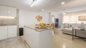 Eine moderne Küche mit Kochinsel, ein Essbereich mit Sofa und Couchtisch sowie ein Wohnzimmer mit Fernseher und Sitzgelegenheiten.