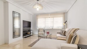 Ein modernes Wohnzimmer mit einer Couch, einem Fernseher, einem Couchtisch und einer außergewöhnlichen Deckenleuchte.