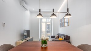 A modern living room with a wooden dining table, a sofa, and a TV. - Cozy 1BR Retreat Steps from Sol & Santa Ana (Madrid)