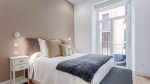 A bedroom with a bed, bedside table, bench, and a view of a balcony. - Cozy 1BR Retreat Steps from Sol & Santa Ana (Madrid)