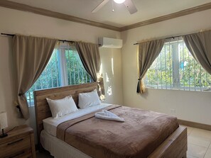 A neatly made bed with a wooden headboard, beige curtains, and a view of greenery outside. - Bay Nassau
SPACIOUS escape to quiet, getaway in Yamacraw Beach, Nassau, Bahamas (Nassau)