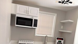 Una cucina compatta con mobili bianchi, un forno a microonde integrato, un piano cottura e un lavandino piccolo.