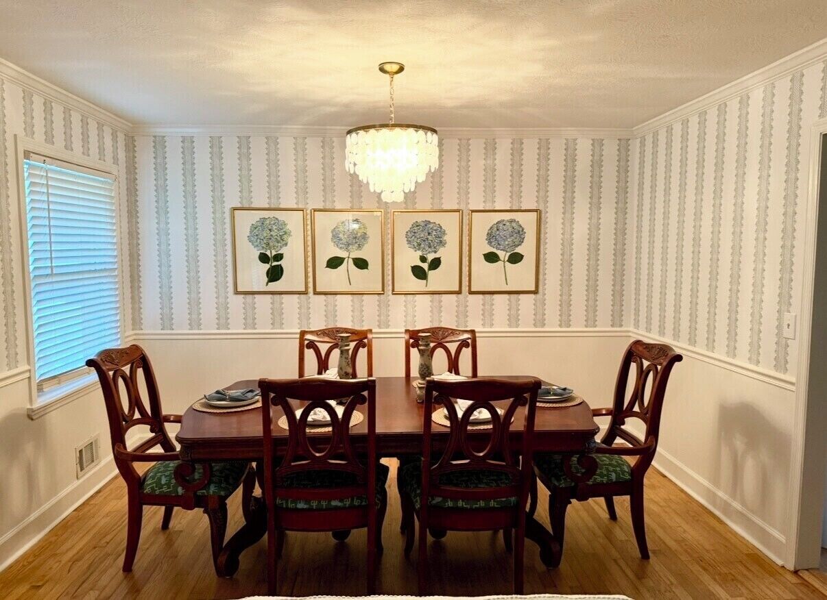 Una sala da pranzo con un tavolo e sedie in legno, un lampadario e opere d'arte floreali incorniciate alle pareti.