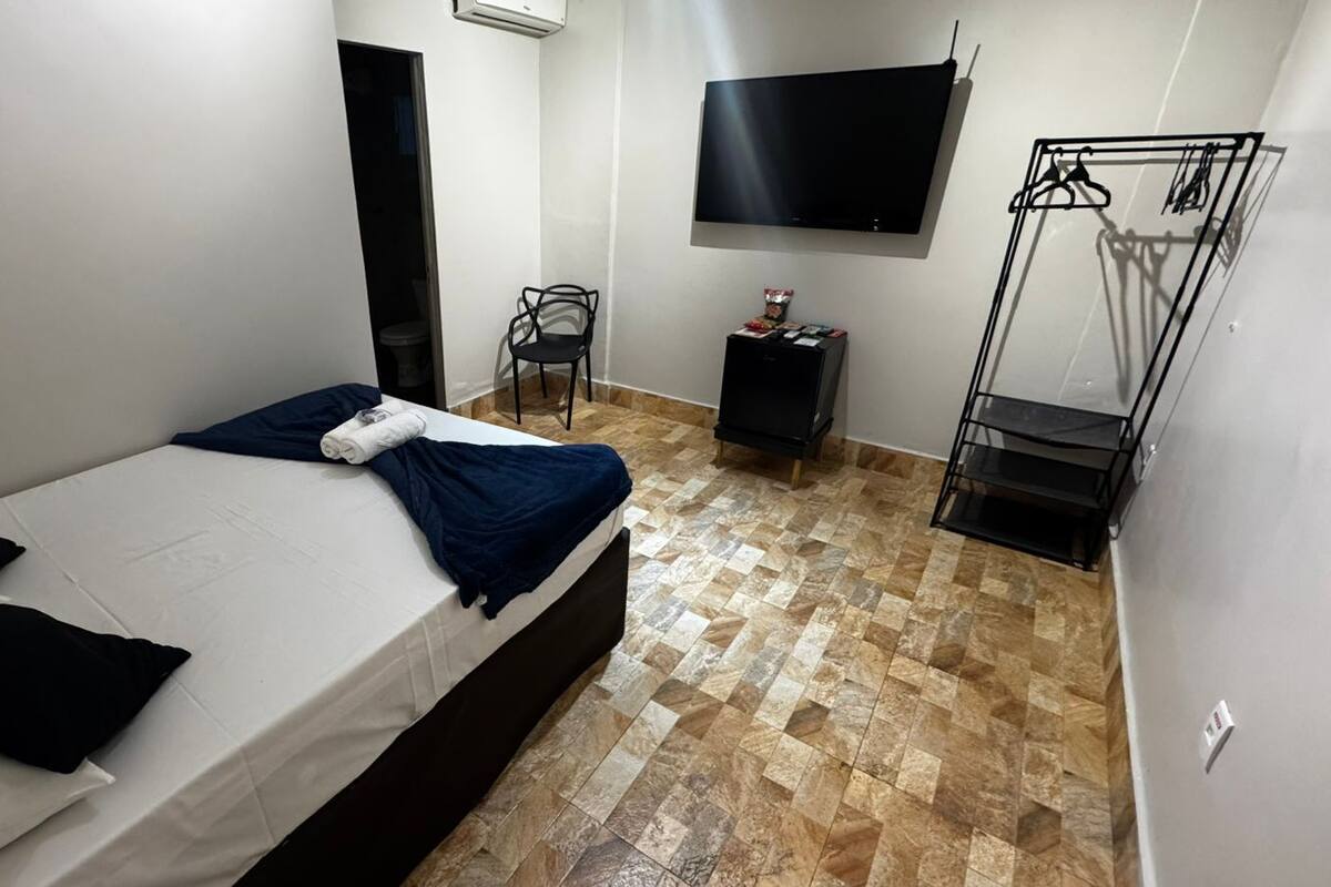 Un dormitorio con una cama, televisión, armario y zapatero.