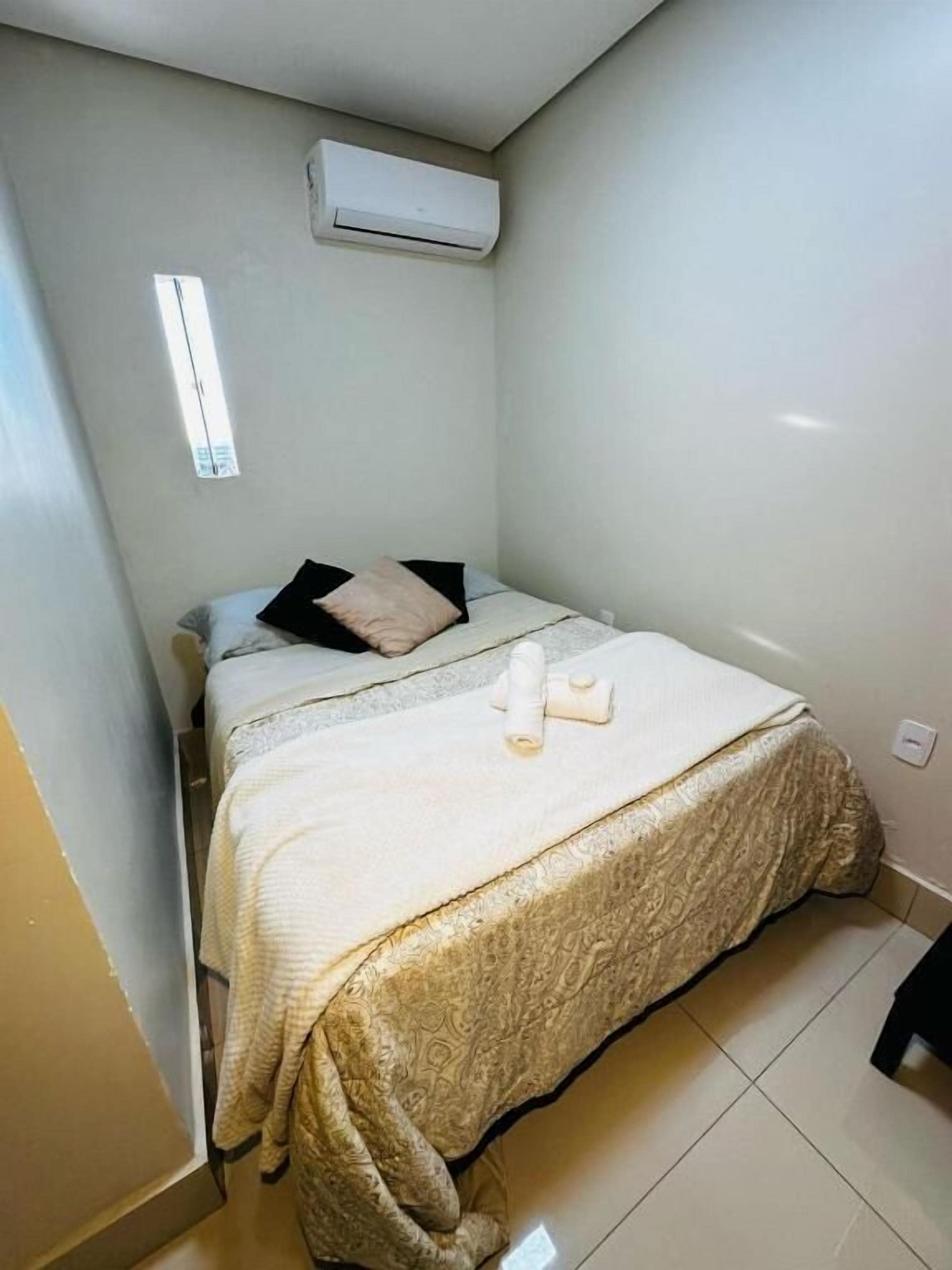 Et lille, rent værelse med en seng, et vindue og en aircondition.