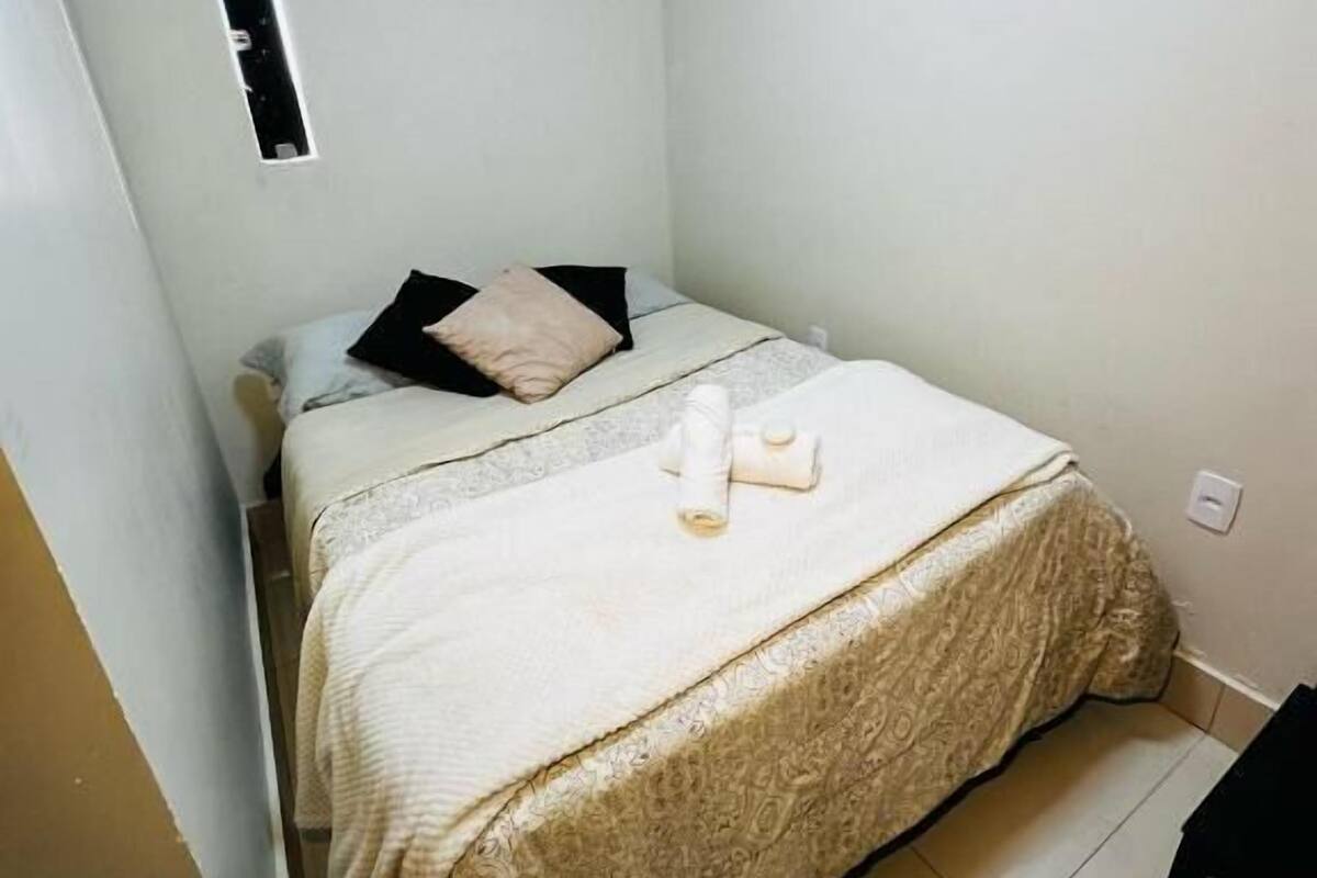 Una habitación pequeña y limpia con cama, ventana y aire acondicionado.
