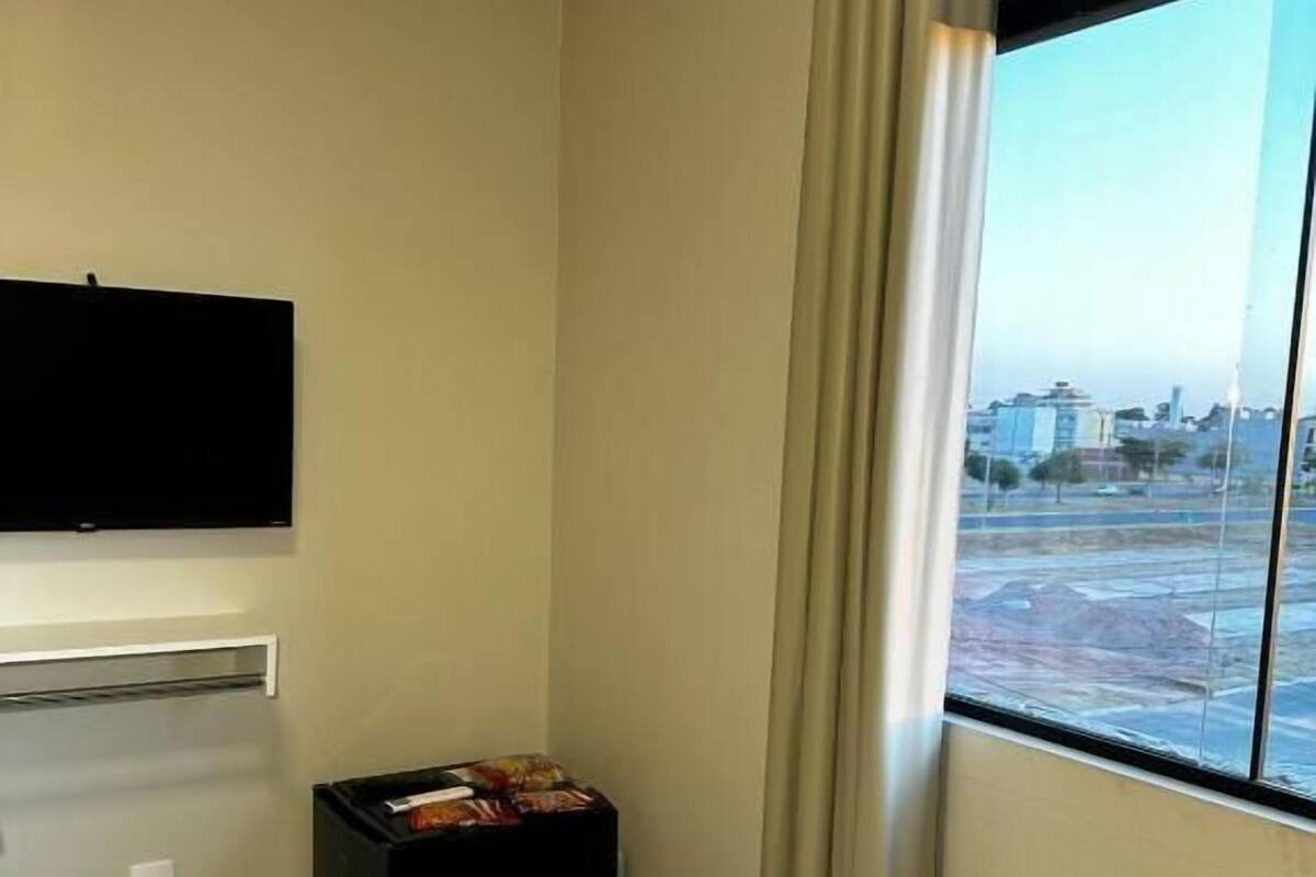 Habitación de hotel con cama, televisor montado en la pared, una mesita con aperitivos y ventana con vistas a edificios.