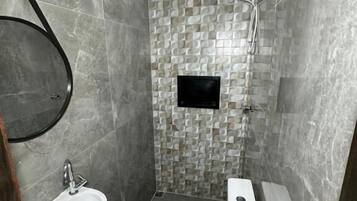 Un baño moderno con piso de baldosas grises, un lavamanos blanco, un inodoro y una zona de ducha.