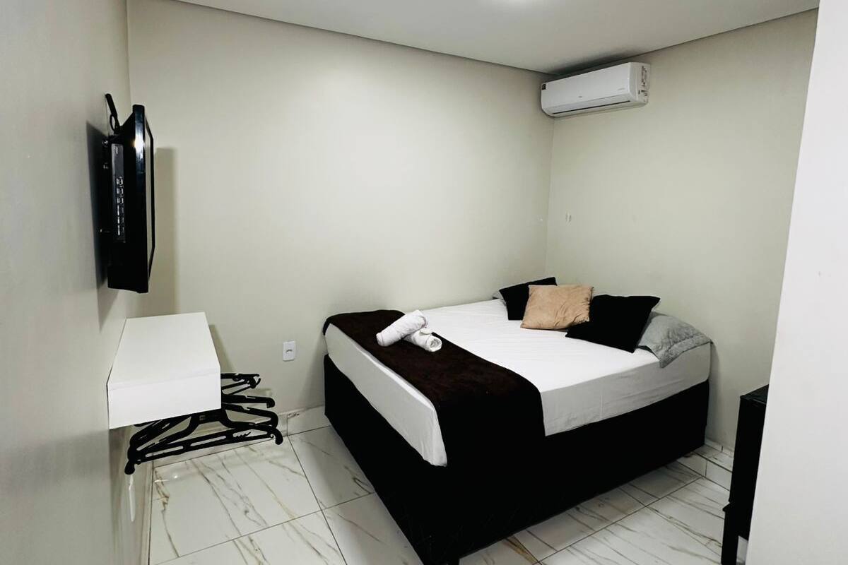 Una habitación pequeña y limpia con cama, televisor, aire acondicionado y una pared blanca.
