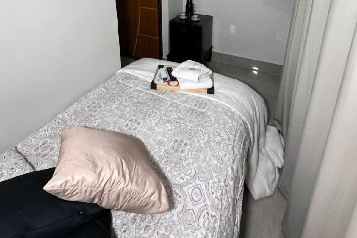 Una habitación de hotel con cama, televisor montado en la pared, una mesita de noche pequeña y una puerta.