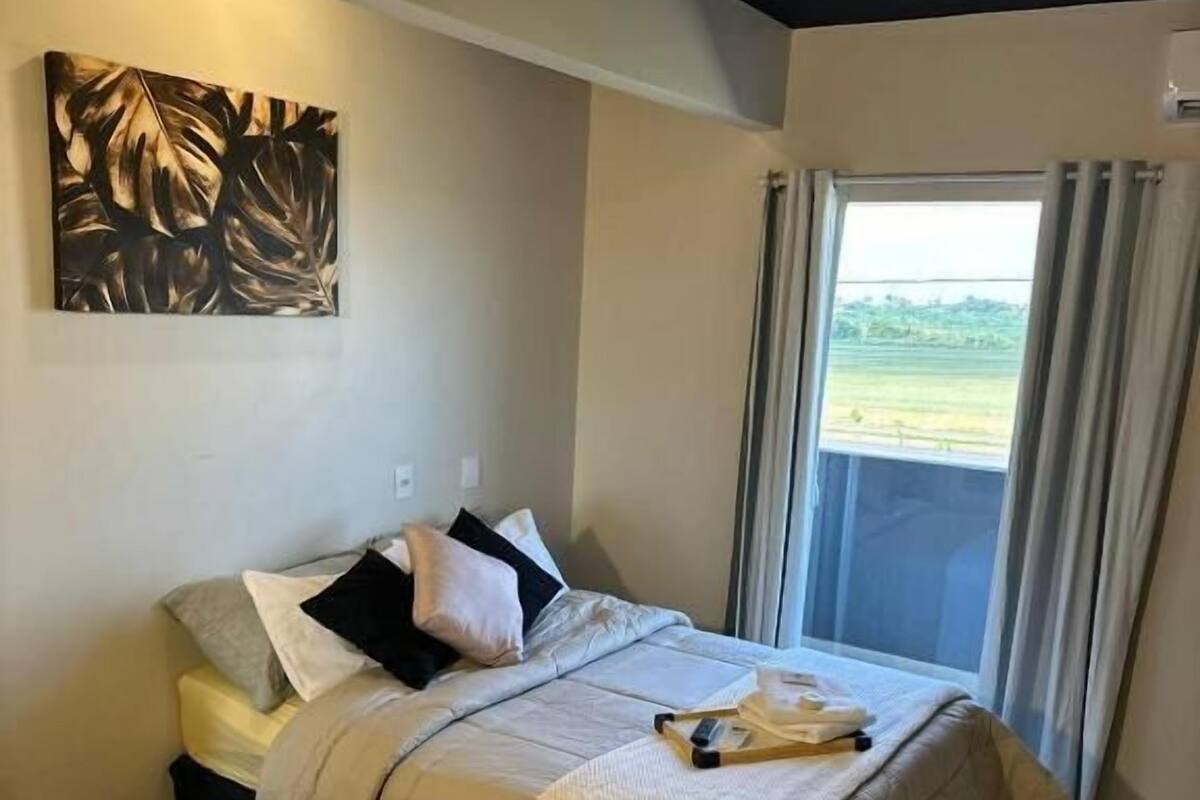 Un dormitorio moderno con una cama grande, un cuadro en la pared y vistas al exterior a través de una ventana.