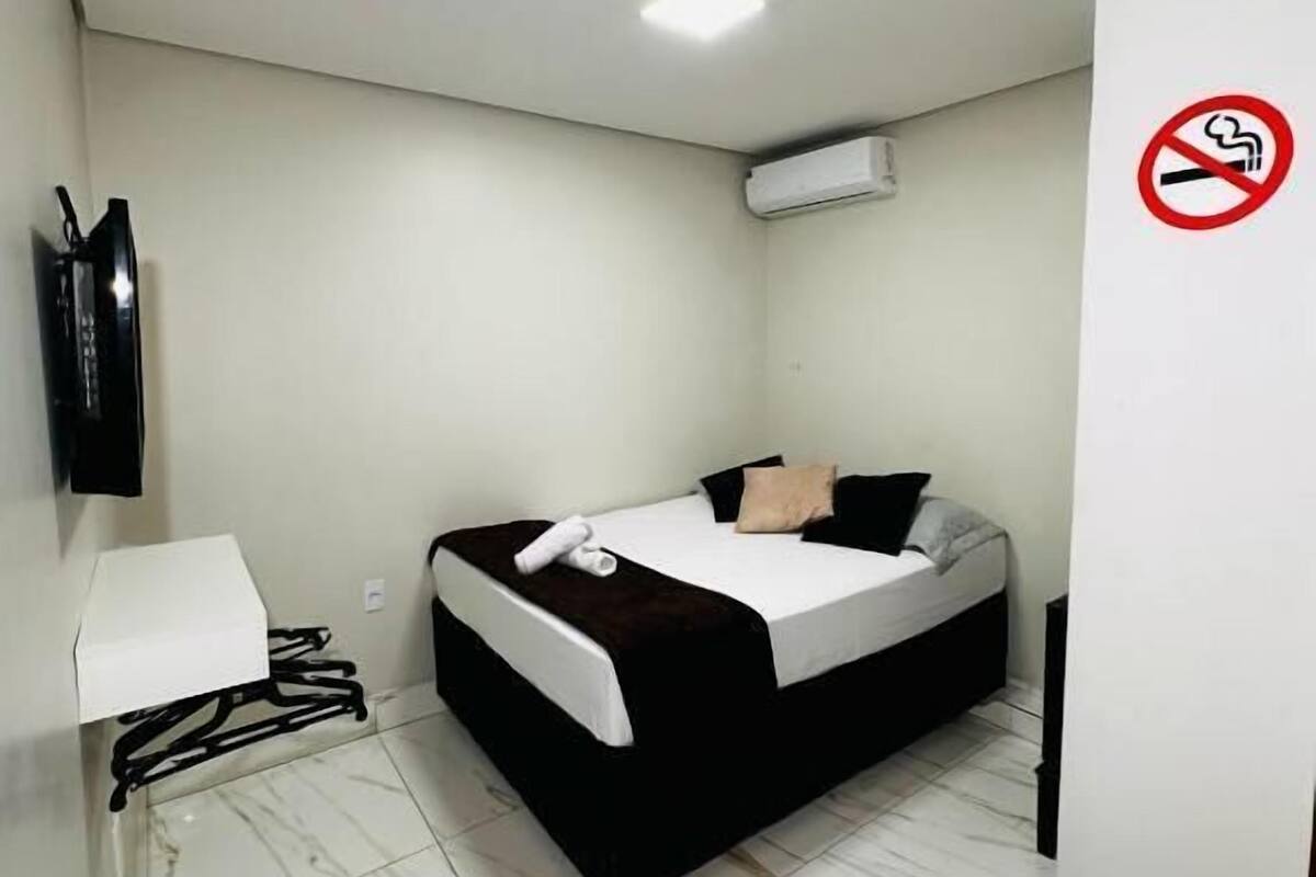 Una habitación pequeña y limpia con una cama, un escritorio y un televisor.