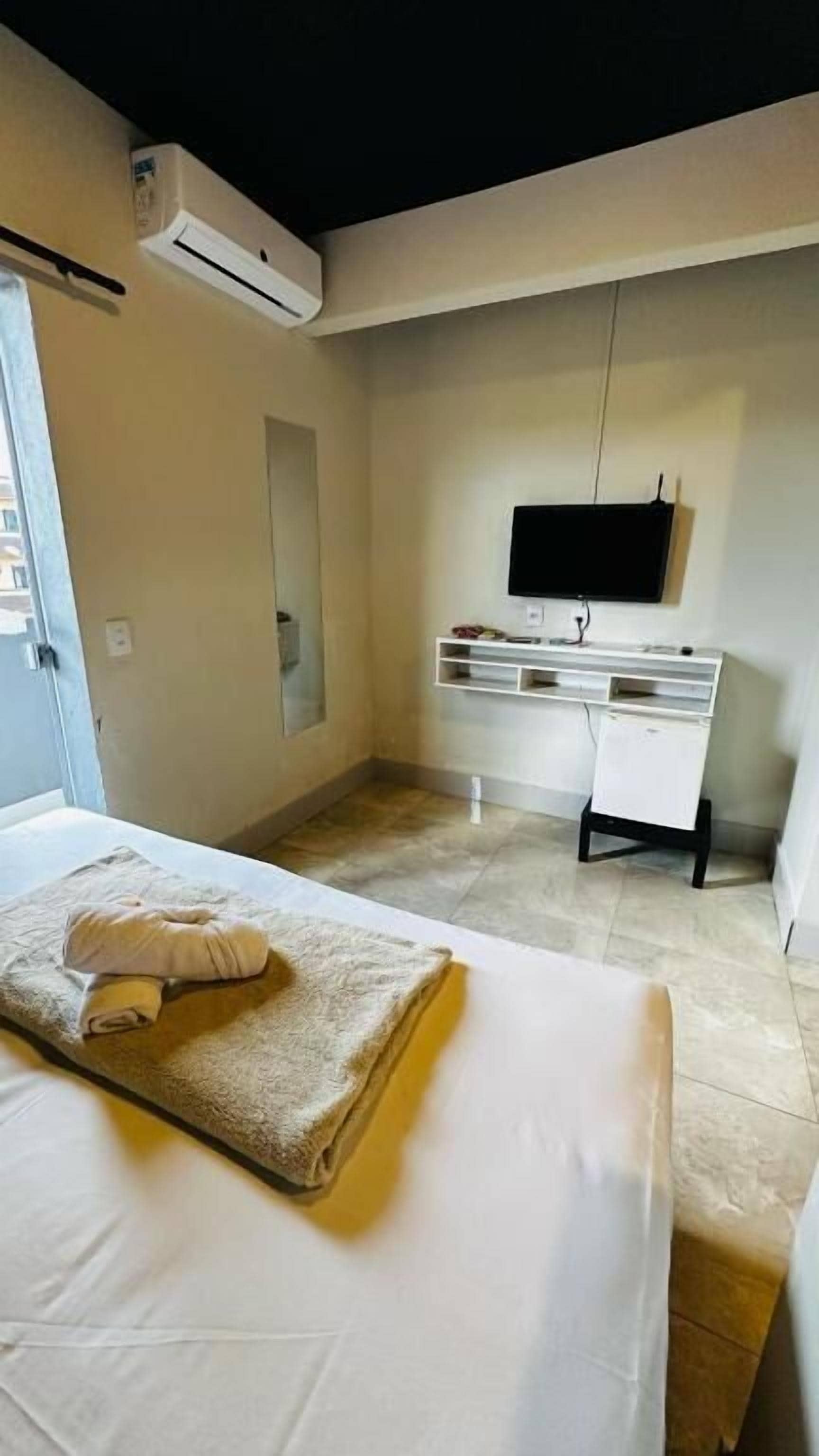 A hotel room with a bed, a desk, a TV, and an air conditioning unit.